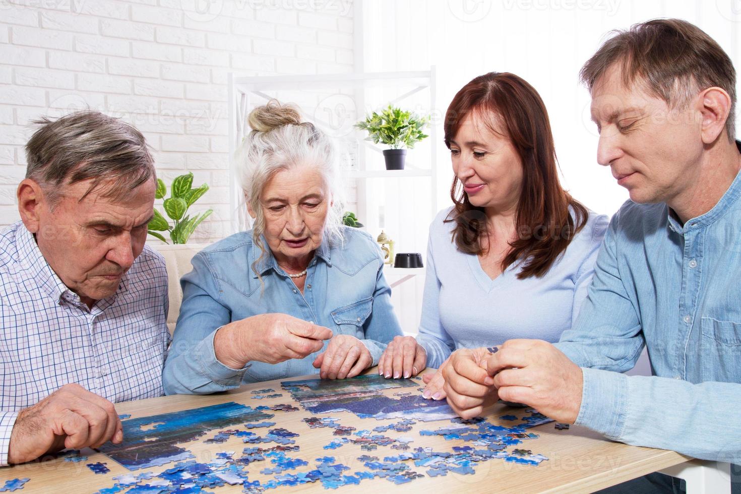 Pareja de ancianos y pareja de mediana edad trabajando juntos en un rompecabezas en casa foto