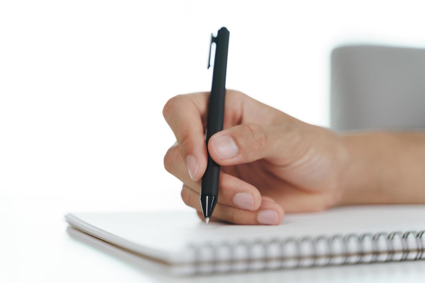 Cerca de la mano del hombre escribiendo en el bloc de notas, cuaderno con bolígrafo sobre la mesa. foto