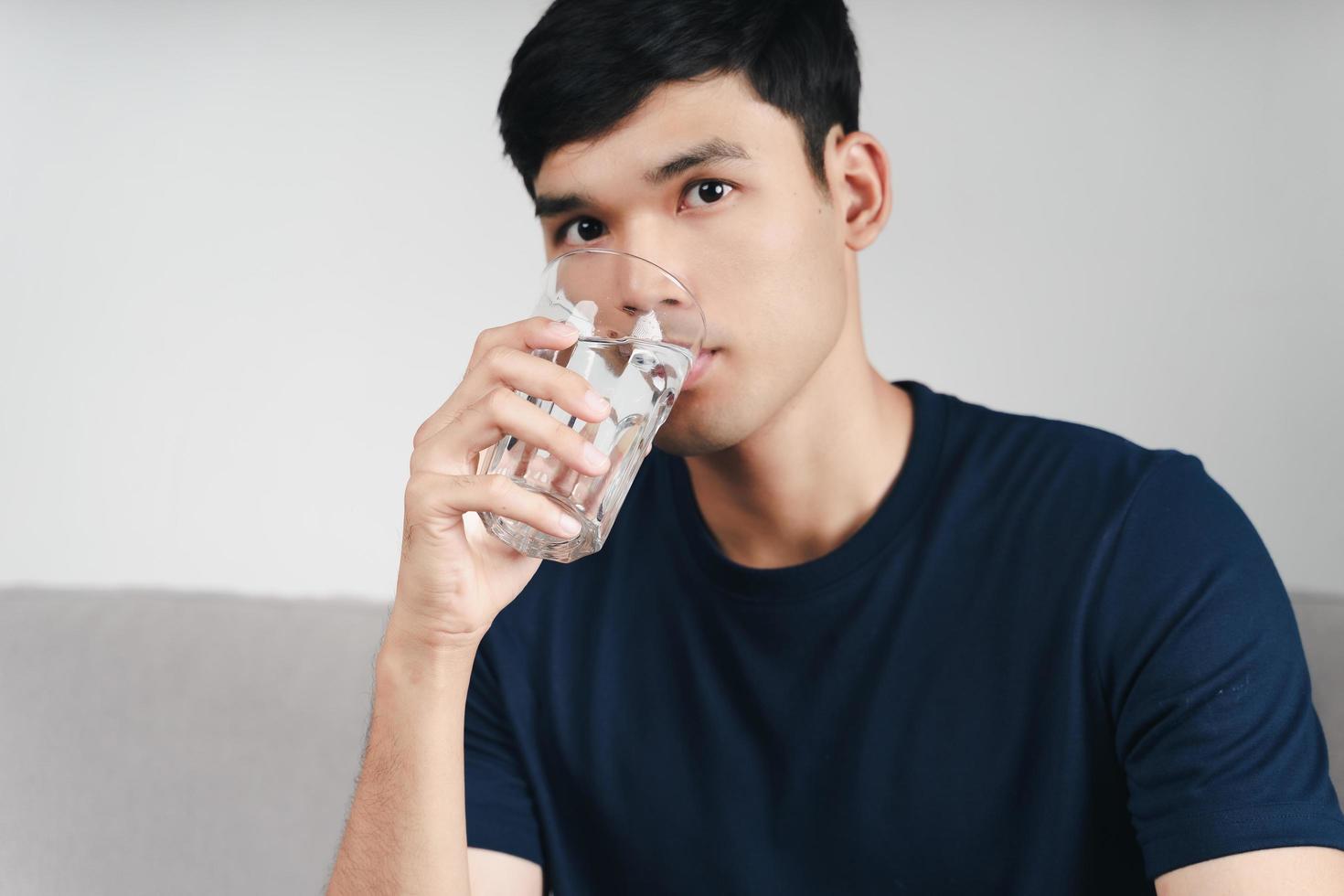 handsome asian man drinking a glass of water on the sofa at living room photo