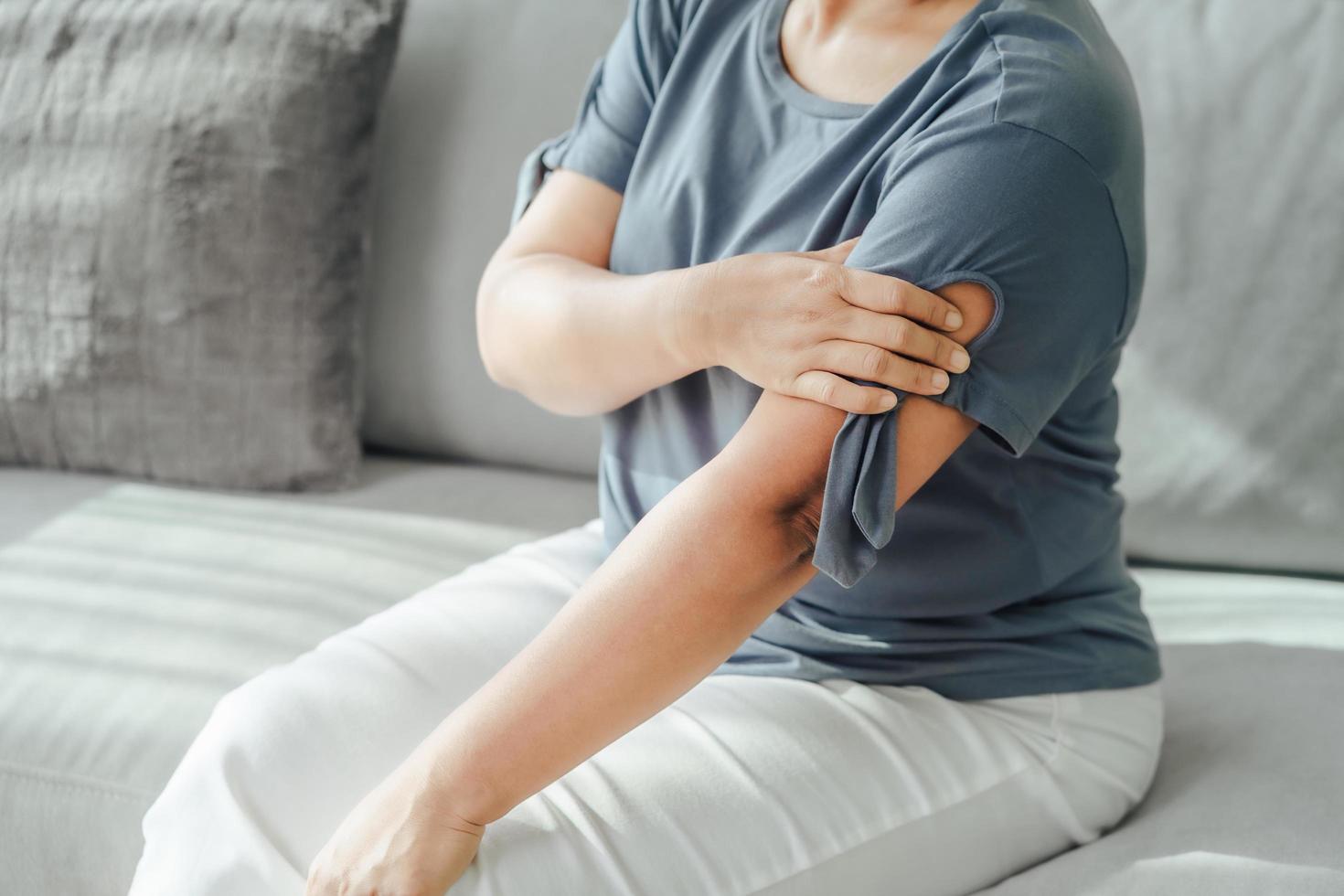 Arms Pain. Woman Suffering From Painful Feeling In Arm Muscles sitting on the sofa. Healthcare and medical concept. photo