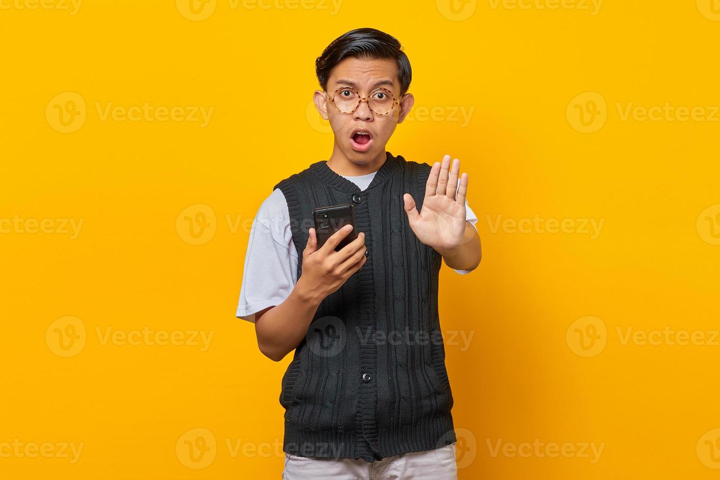 Surprised Asian young man with open mouth holding smartphone and doing stop motion with palms photo