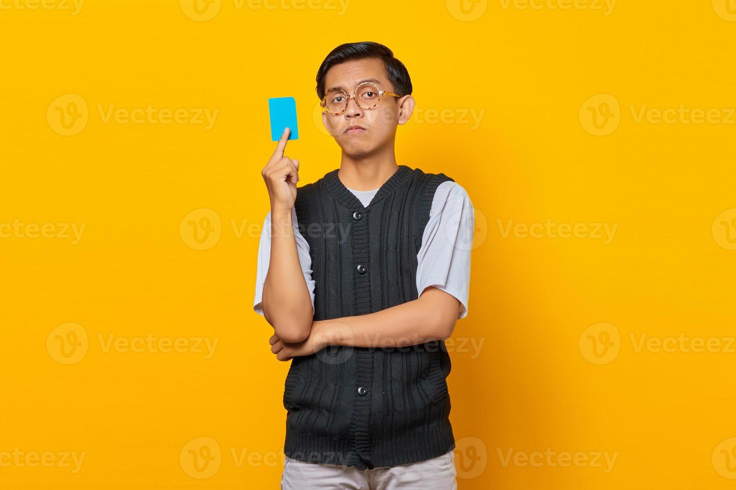 Portrait of shocked young Asian man showing credit card on yellow background photo