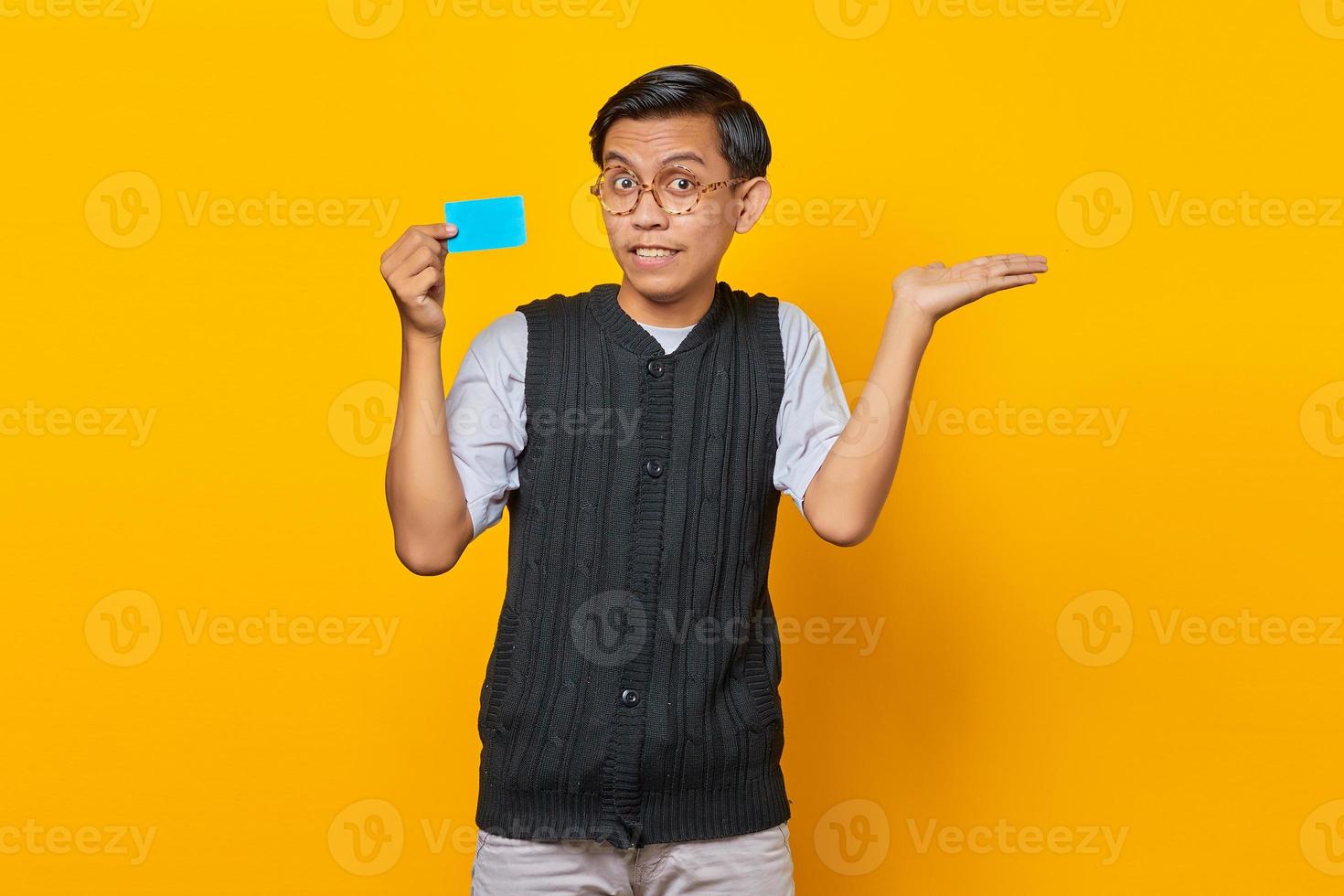 Portrait of smiling handsome young man showing copy space in palm and holding credit card photo