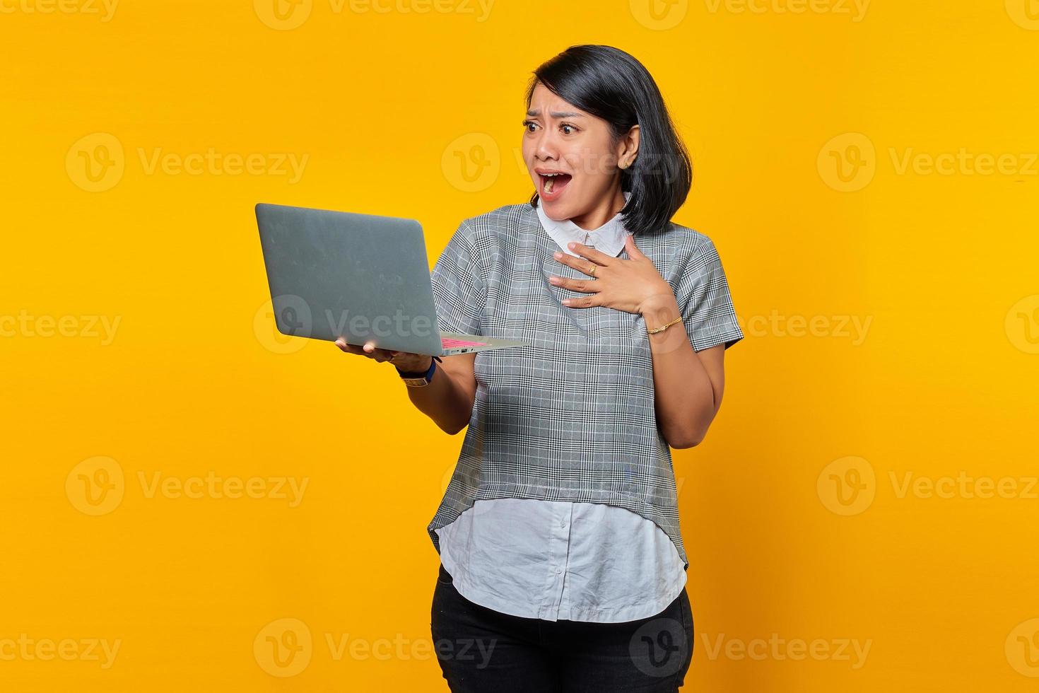 Retrato de mujer asiática emocionada que recibe el correo electrónico entrante en el portátil sobre fondo amarillo foto