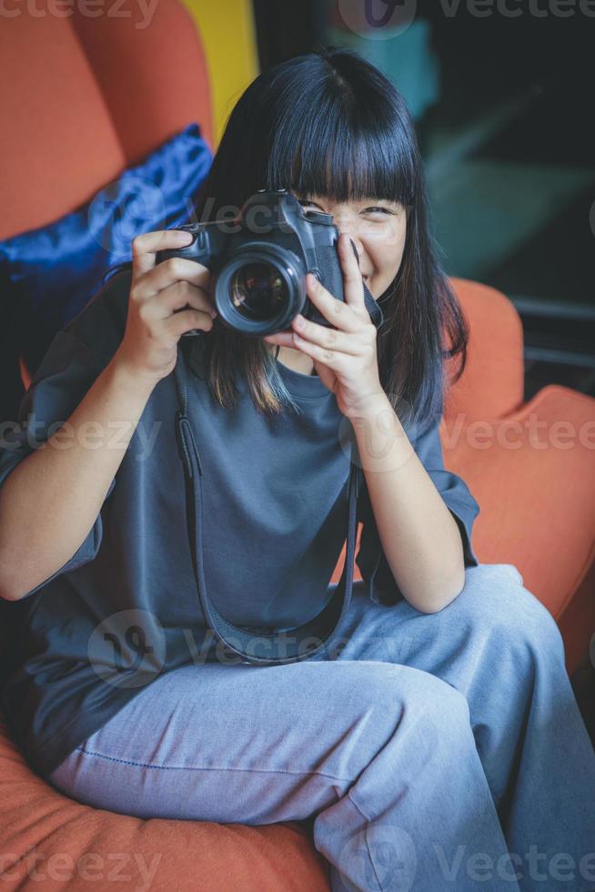 Adolescente asiático sentado en el sofá y tomando una fotografía con una cámara réflex digital foto