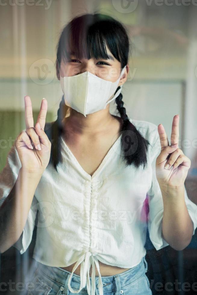 mujer asiática, llevando, protección, mascarilla, posición, atrás, casa, espejo, puerta, señal, victoria, mano foto