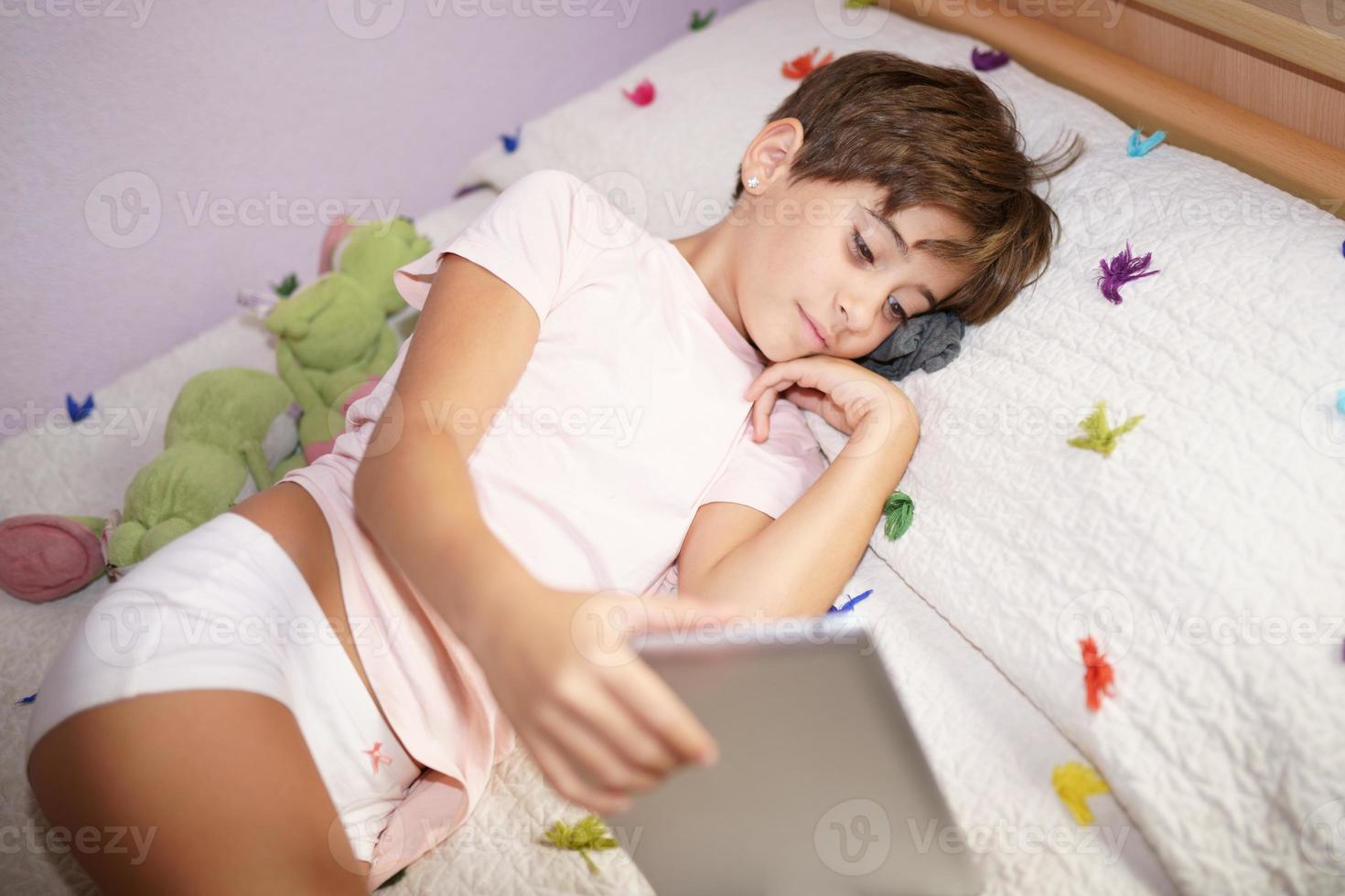 Cute girl using a tablet computer in her bedroom photo