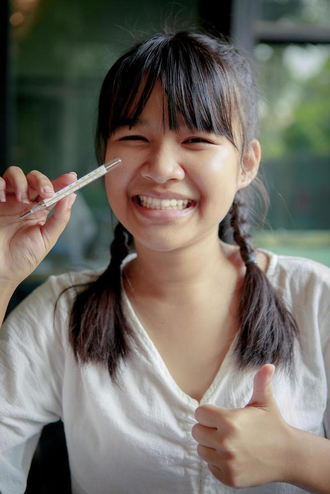 Adolescente asiático con dientes sonriendo y sosteniendo el termómetro corporal en la mano foto