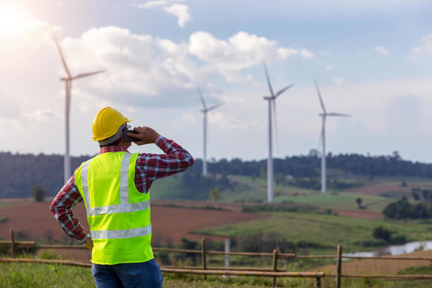 Technician Engineering man standing mobile calling partner and looking wind turbines clean energy project for produce electricity service photo