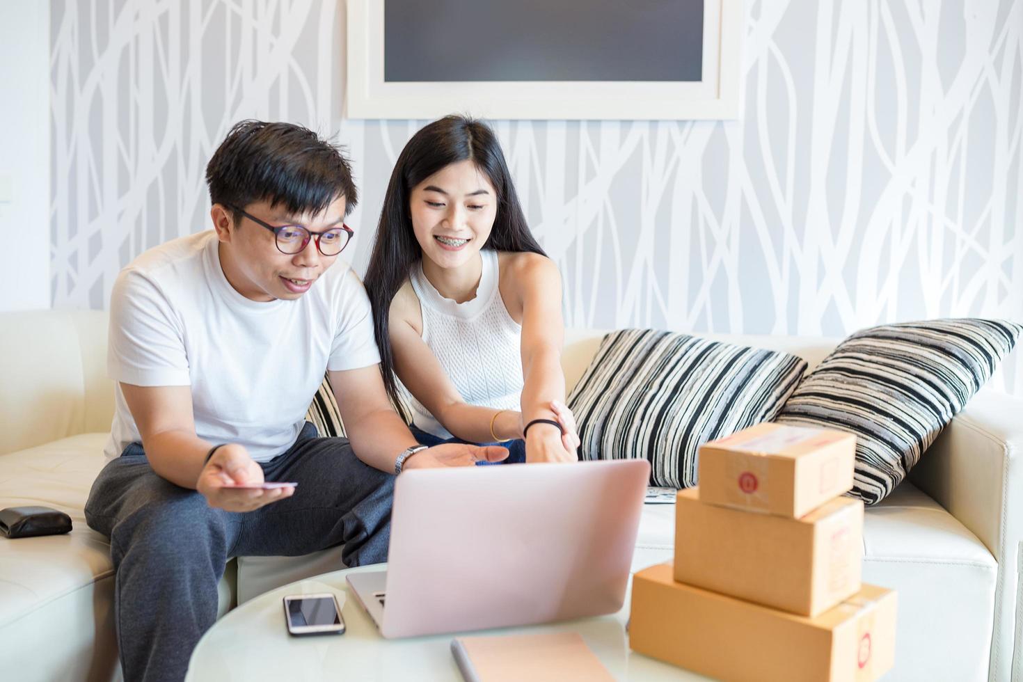 Feliz pareja joven comprando juntos en línea en la computadora portátil y pagar con tarjeta de crédito y muy feliz en el apartamento de ellos. este es el estilo de vida de los jóvenes asiáticos. foto