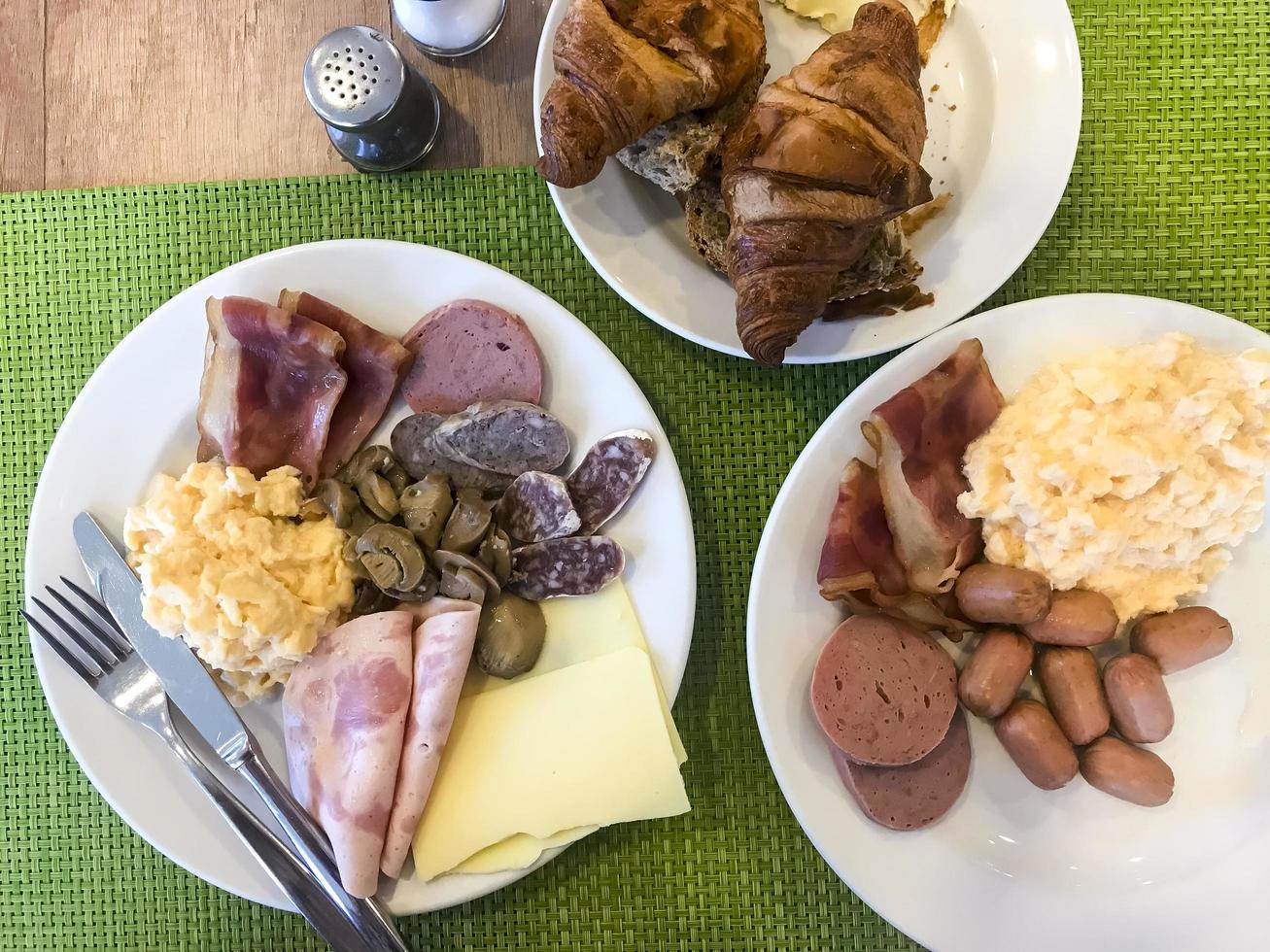 vajilla en la mesa del desayuno. huevos revueltos, tortilla, paté, croissants, champiñones, tocino crujiente, salchichas. foto