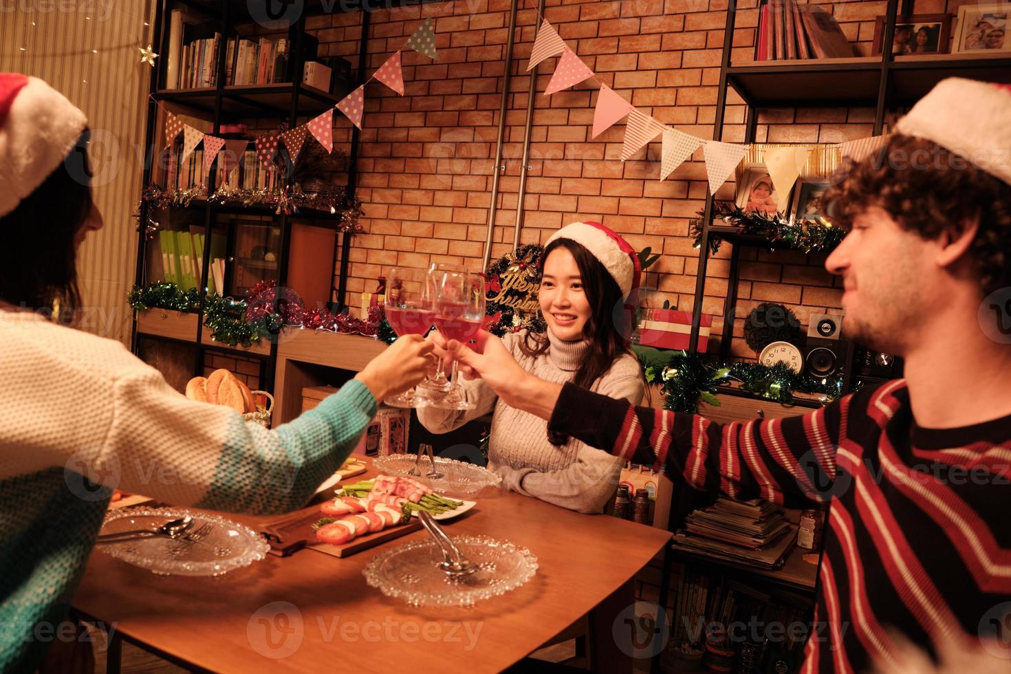 Happiness family and friends are celebrating, raising glasses and a cheerful smile with drinks, enjoy eating foods in home's dining room, decorated for Christmas festival party and New Year's Day. photo