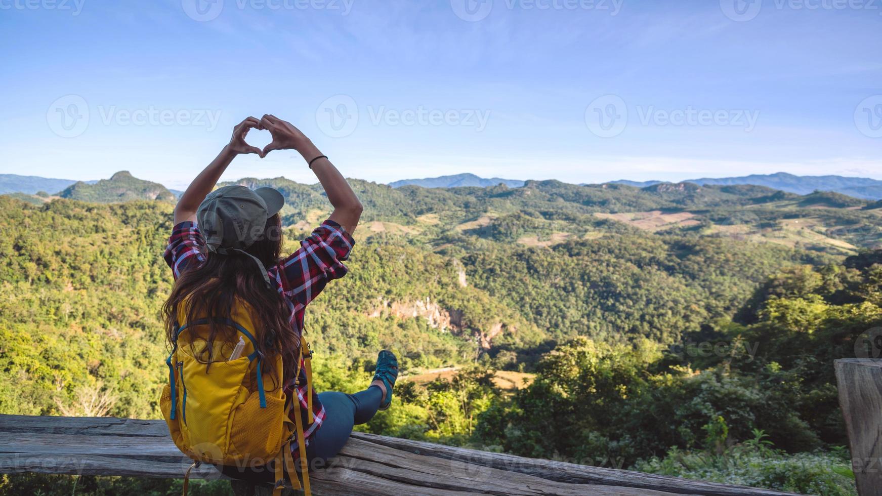 Joven turista con mochilas felices de viajar levantó la mano para hacer una forma de corazón y disfrutar del paisaje natural de la montaña. foto