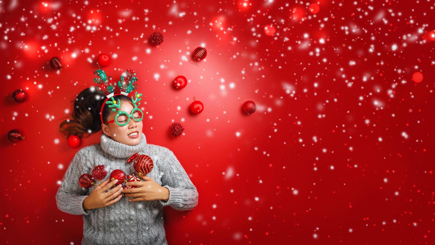 Christmas New Year. Young Woman dressed in warm sweater with  Props ball red with christmas ornaments in Holiday on shine red background. Concept merry christmas. photo