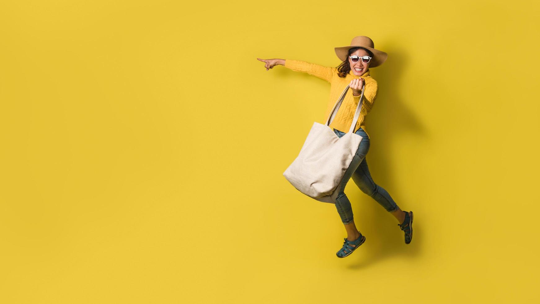 Portrait of an excited beautiful girl wearing dress and sunglasses holding shopping bags. Cheerful young woman with handbag on yellow background. Shopaholic shopping Fashion. photo