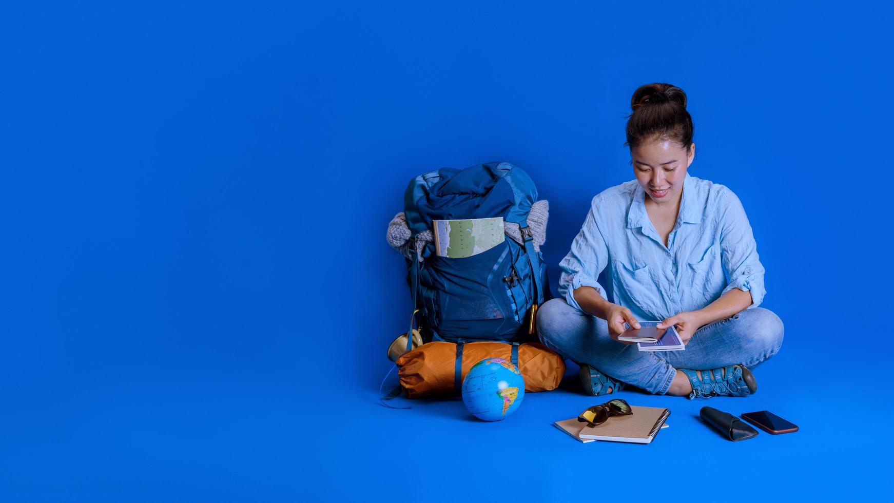 vacaciones de planificación turística con la ayuda del mapa del mundo con otros accesorios de viaje alrededor. viajero mujer con maleta sobre fondo de color azul. mochila de viaje conceptual foto