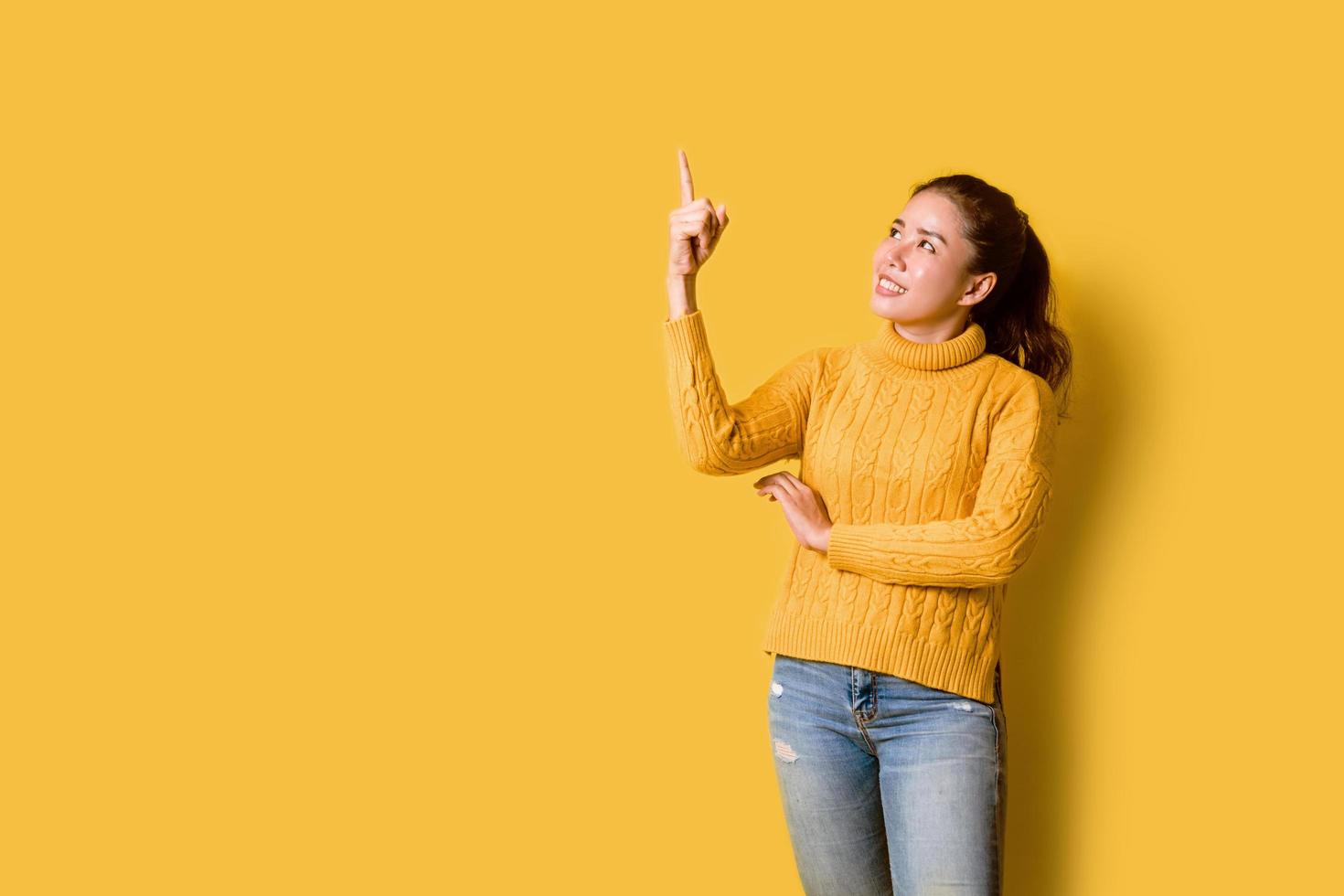 beautiful girls smiling happy pointing upwards in studio yellow background. photo