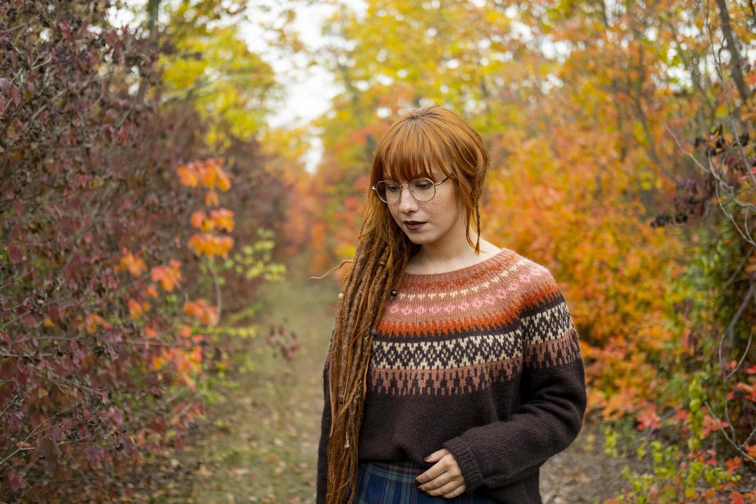 Young woman with red dreadlocks and wearing a sweater in the beautiful autumn forest photo