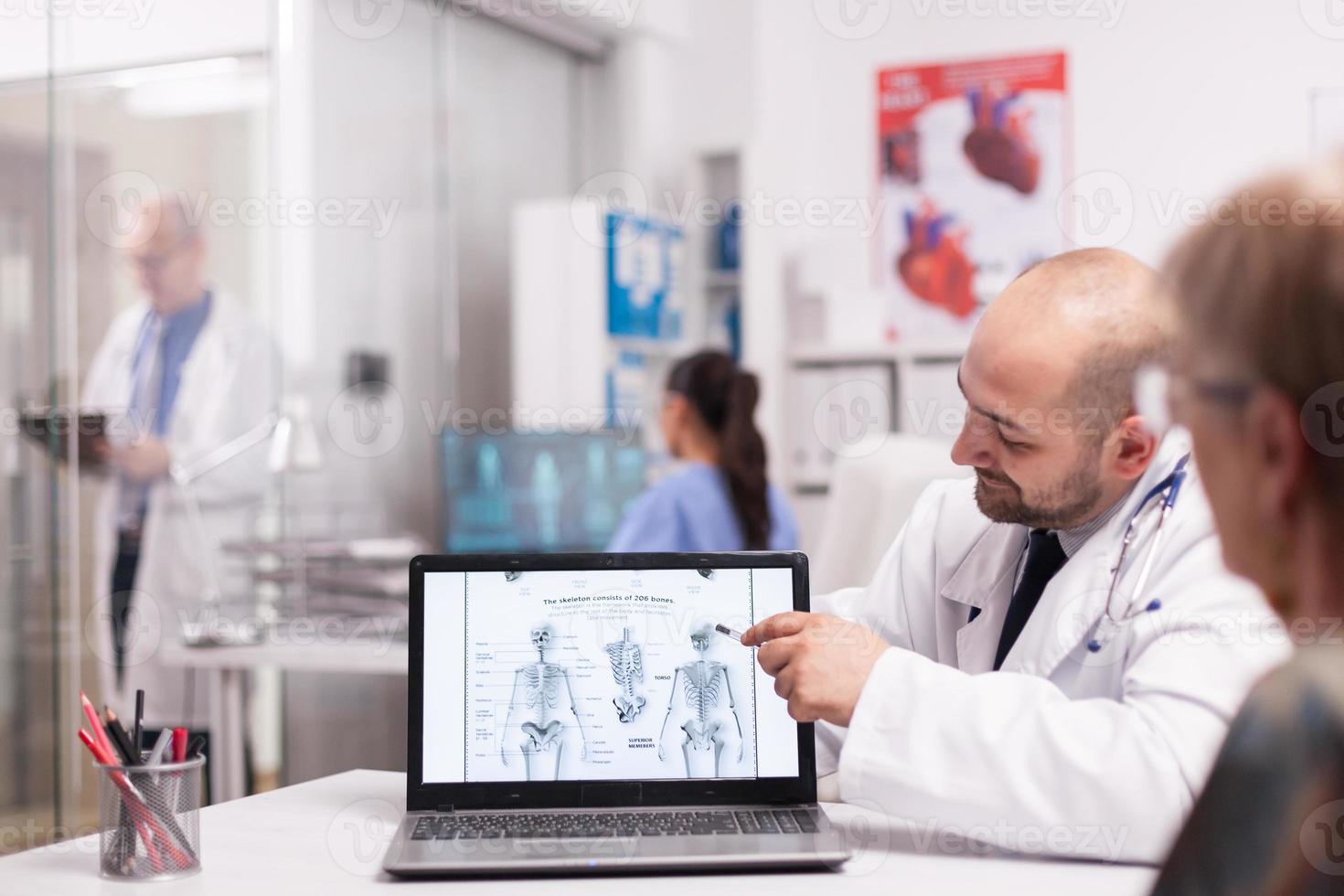 Doctor pointing at human skeleton on laptop photo