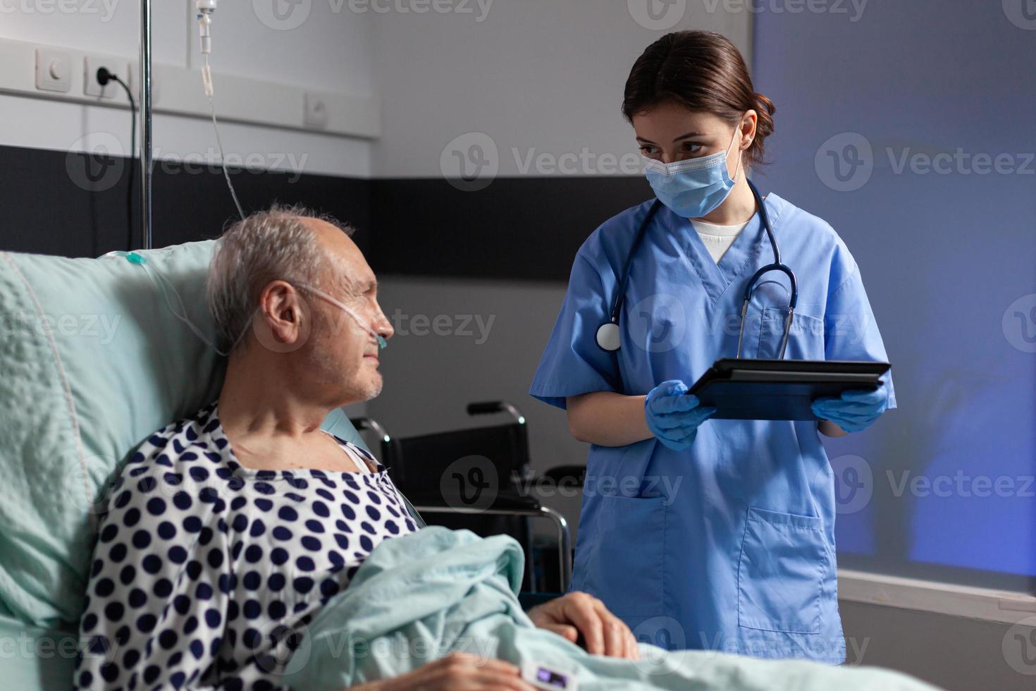 Asistente médico con máscara de protección comprobando el tratamiento del hombre mayor foto