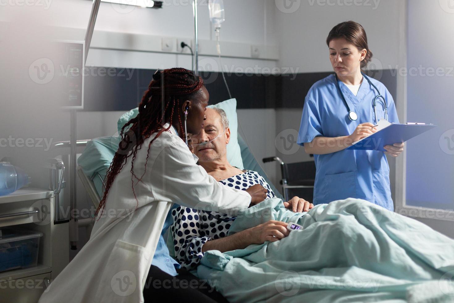 Médico africano especialista con estetoscopio escuchando corazón de hombre mayor foto