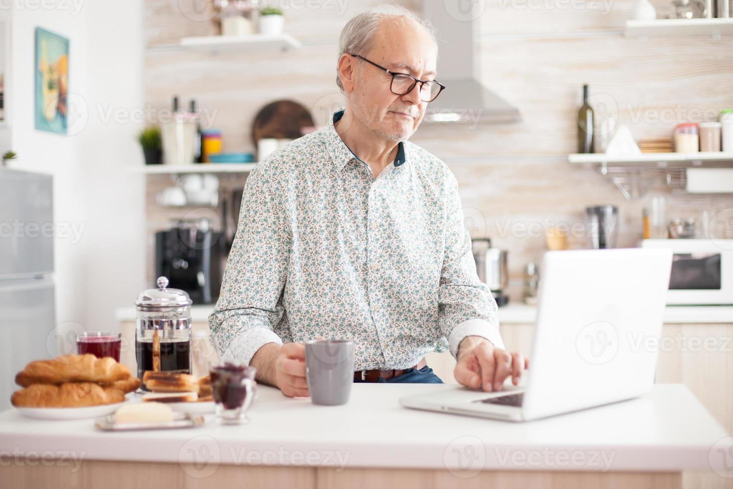 hombre mayor, usar la computadora portátil, en la cocina foto