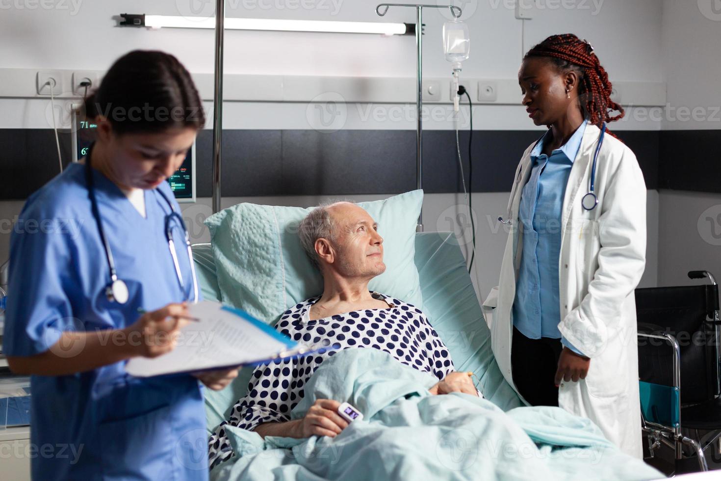African doctor in hospital room discussing with sick senior man photo