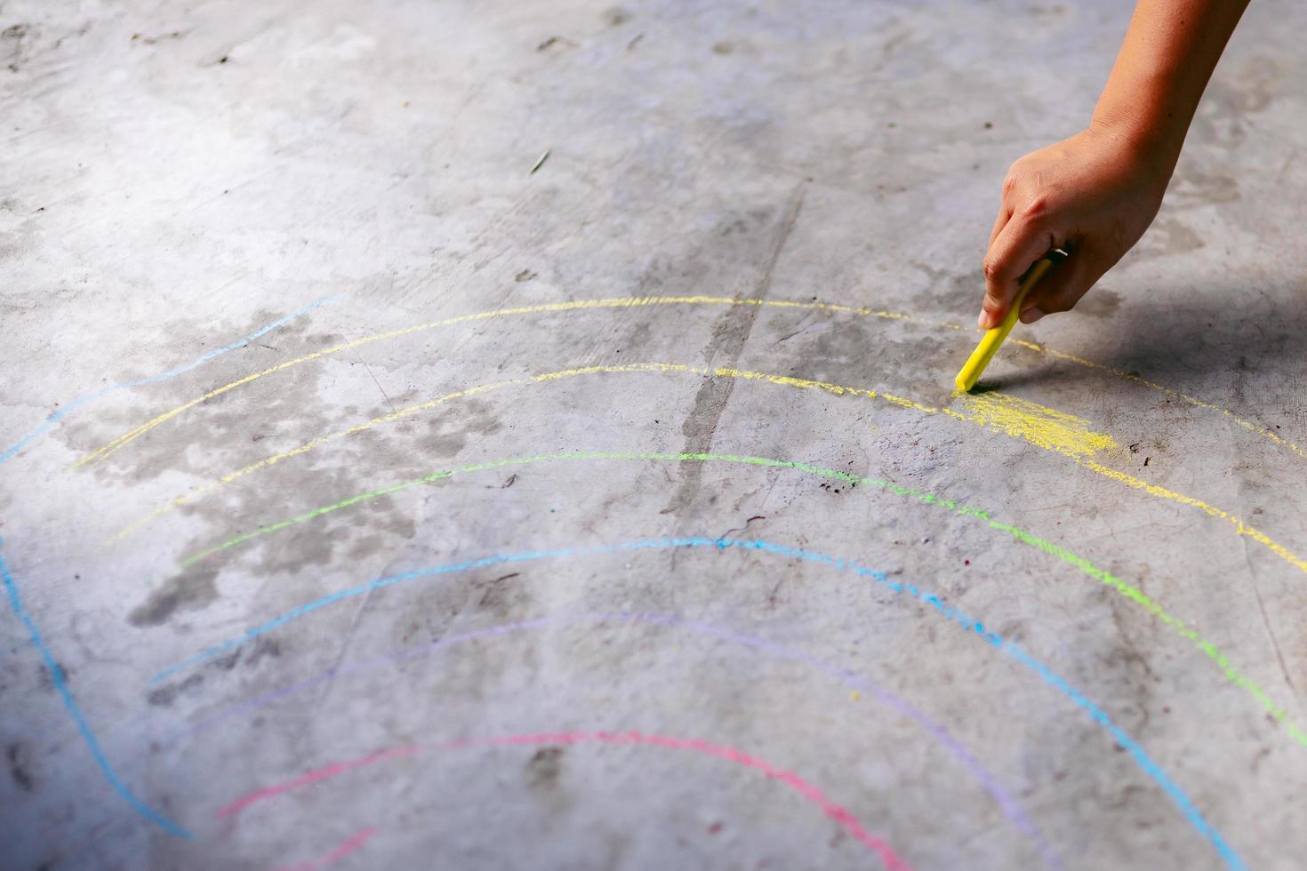 Person hand holding chalk stick draws rainbow like drawings on concrete floor. photo