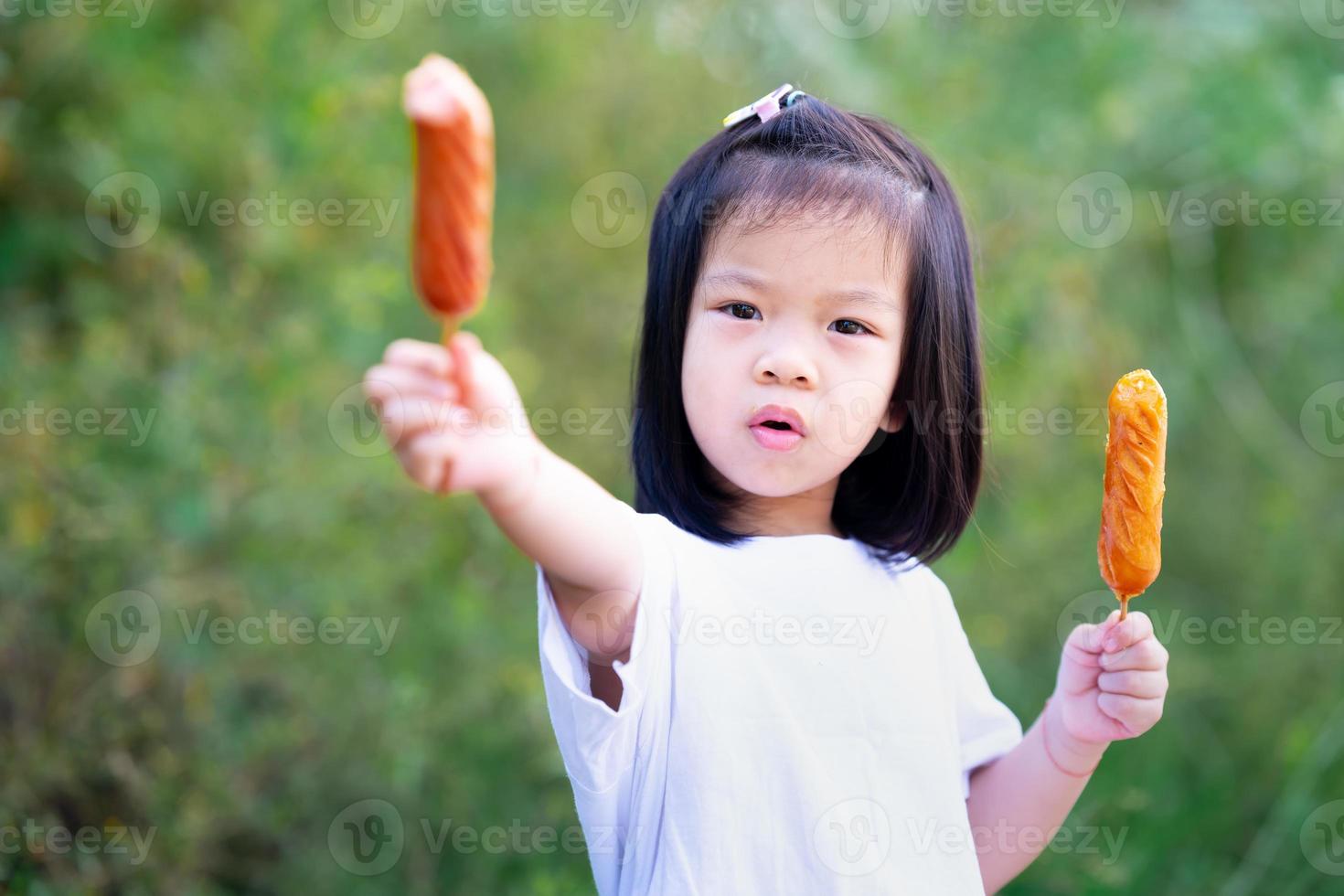 Cute girl holds two sausage with her two hands. Child eat foods that are easy to eat. photo