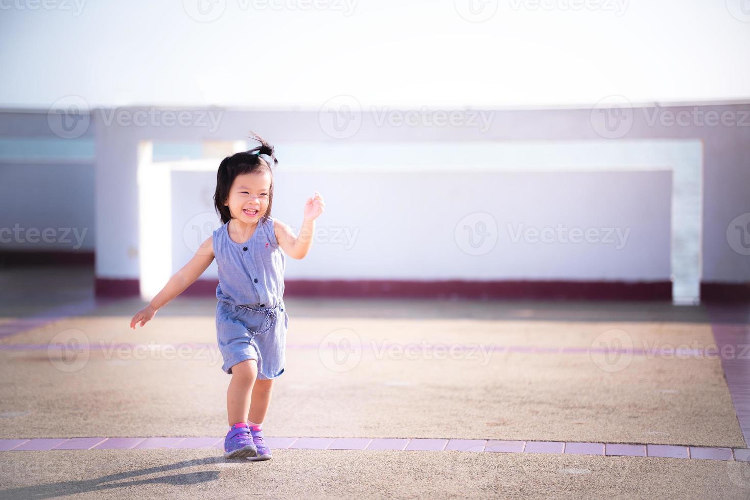 alegre chica asiática jugando y bailando bajo el cálido sol con una sonrisa brillante. concepto de bebé feliz. bebé de 2 años y 9 meses. foto