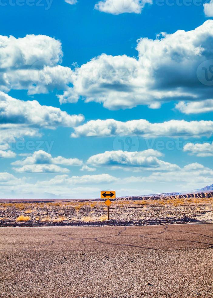 señal direccional en el desierto con un cielo azul escénico y un amplio horizonte. concepto de viaje, libertad y transporte. foto