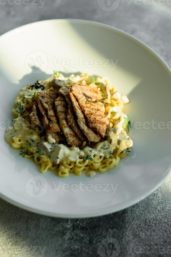 plato con trozos de carne, pasta, verduras, salsa de foie gras foto