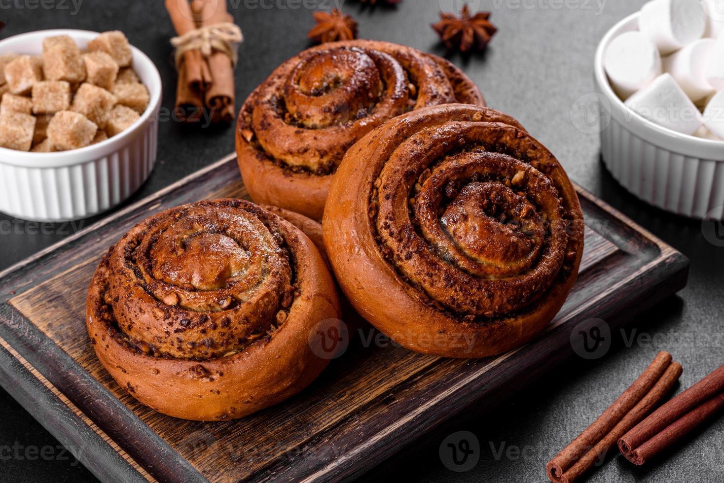 Rollo de canela recién horneado con especias y relleno de cacao sobre un fondo negro foto