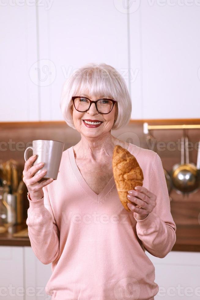 Senior elegante mujer desayunando comiendo croissant y tomando café. hábitos, concepto de rituales foto