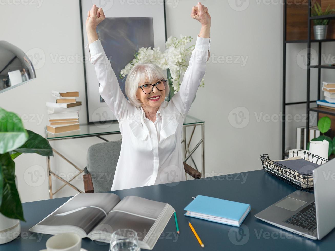 Mujer de cabello gris hermosa senior en blusa blanca feliz en la oficina. trabajo, personas mayores, problemas, éxito, encontrar una solución, concepto de experiencia foto