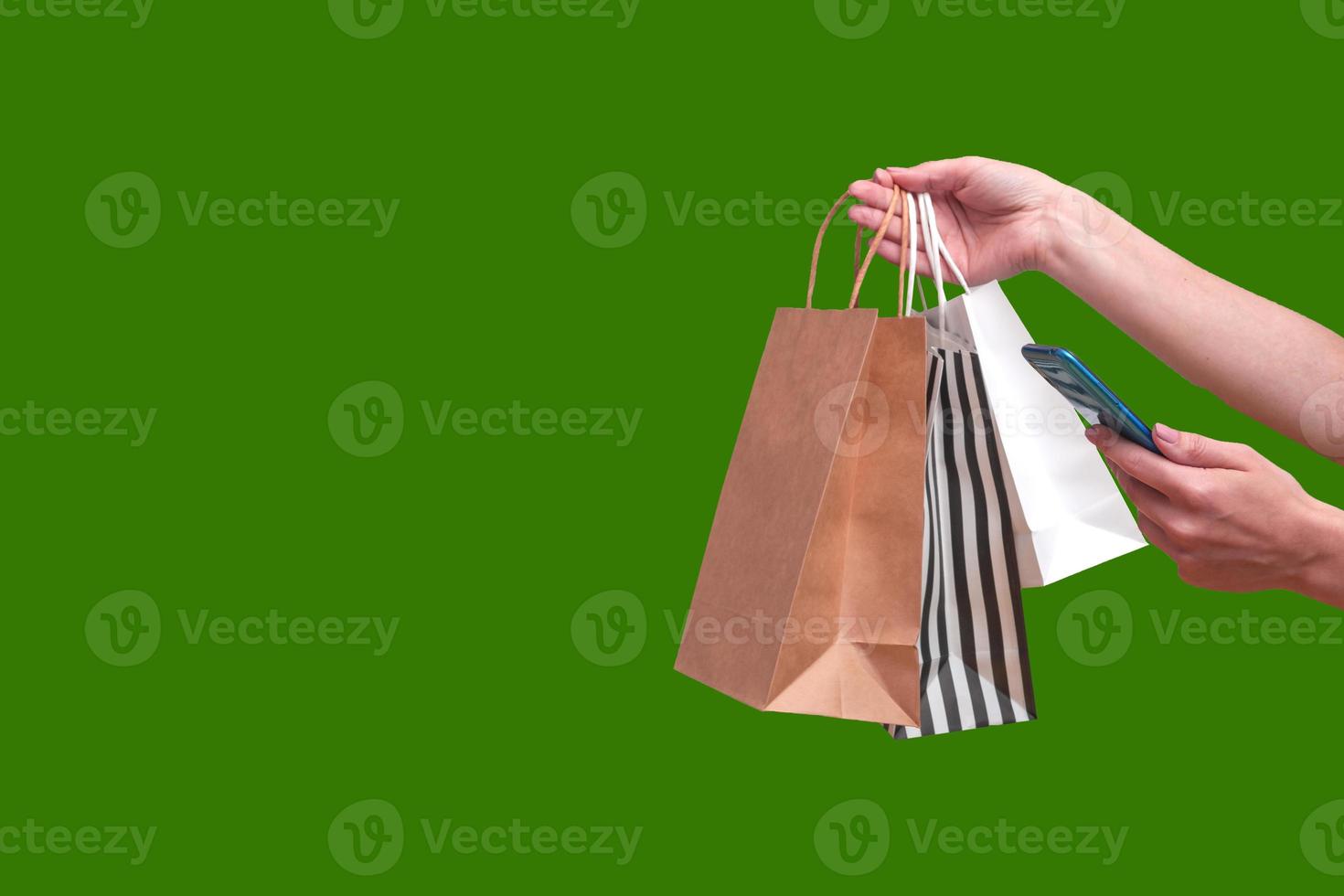 mujer de compras en línea desde un teléfono móvil. manos femeninas con paquetes aislados sobre fondo verde, espacio de copia de cerca. foto
