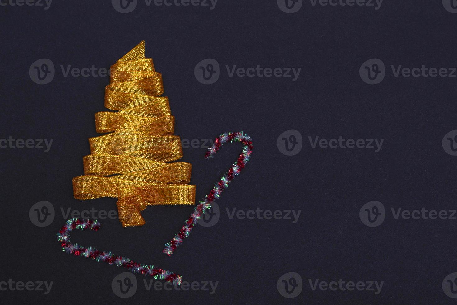 Christmas concept. Golden Christmas tree made of ribbons with a staff on a black background with copy space on top. Template for postcards, packaging, advertising. photo