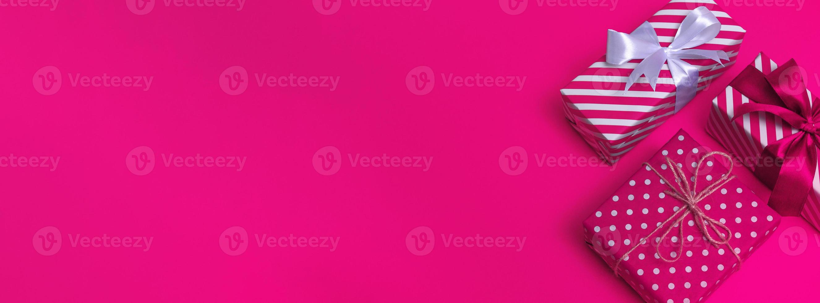 An overhead view of a white gift with pink stripes and white polka dots on a pink background with copy space. Banner photo
