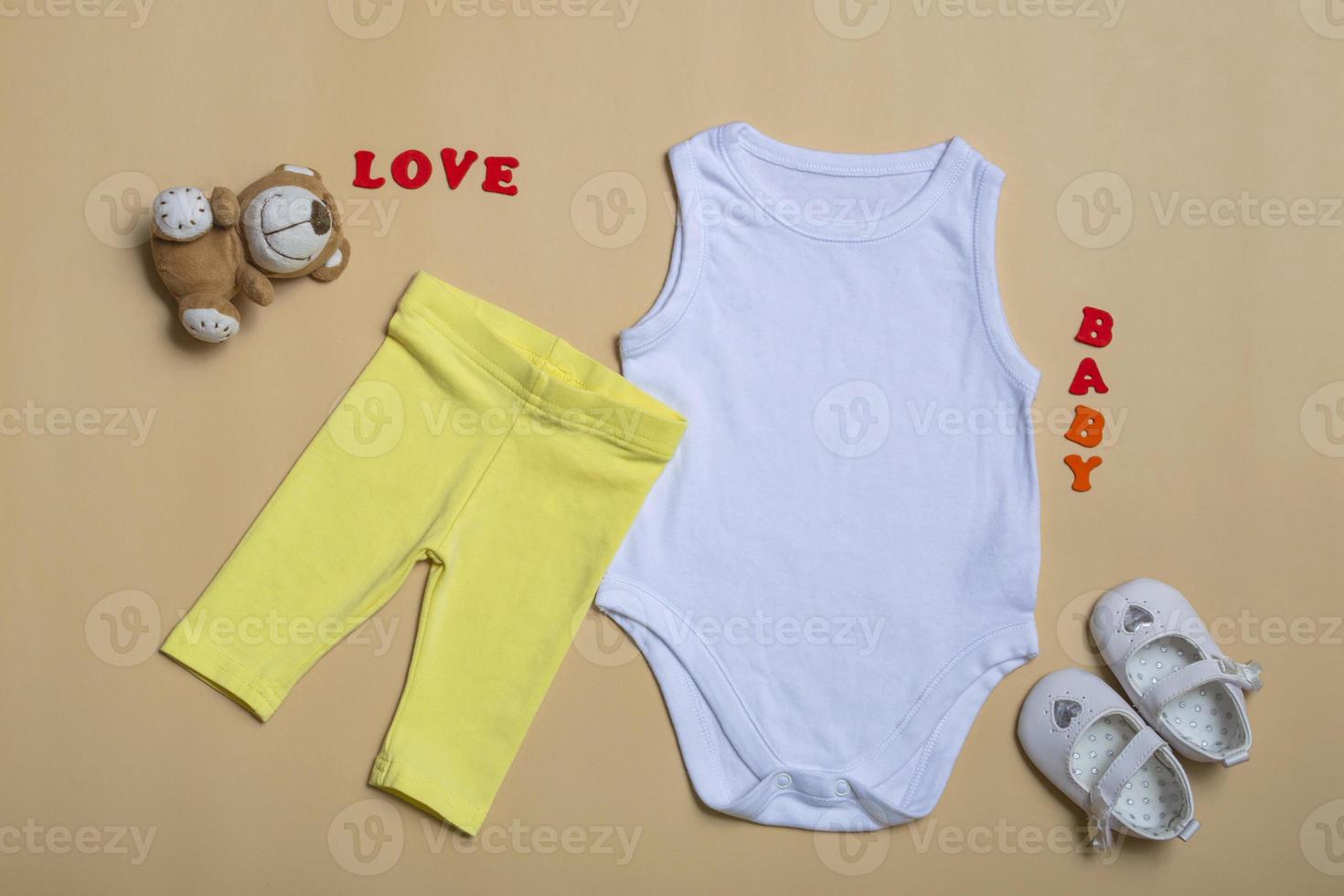 mockup Flat Lay white baby shirt, yellow pants, white shoes with toys on a colored background. Layout for design and placement of logos, advertising. photo