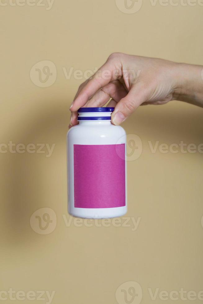 primer plano, sobre un fondo beige. la niña tiene vitaminas en una botella blanca en la mano. vitaminas para inmunidad, recuperación. vitaminas para la belleza. lugar para el texto. foto vertical
