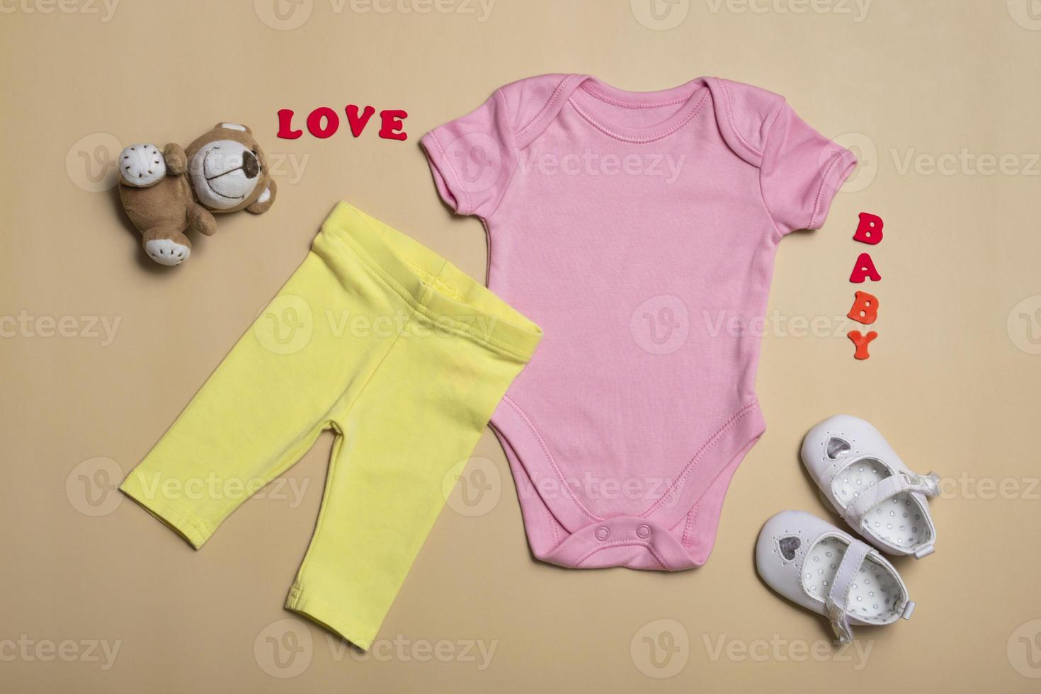 Close-up top view. Mockup blank pink bodysuit, yellow pants and white newborn sandals on a beige background, with copy space - perfect baby clothes mockup template photo