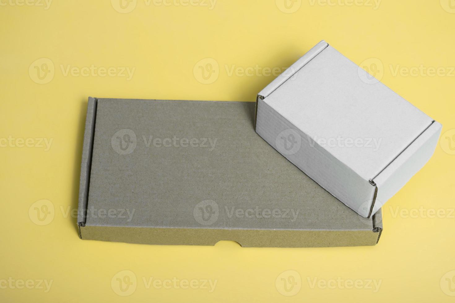maqueta de caja de cartón blanca y caja de cartón marrón sobre fondo amarillo. lugar para el texto. formulario foto