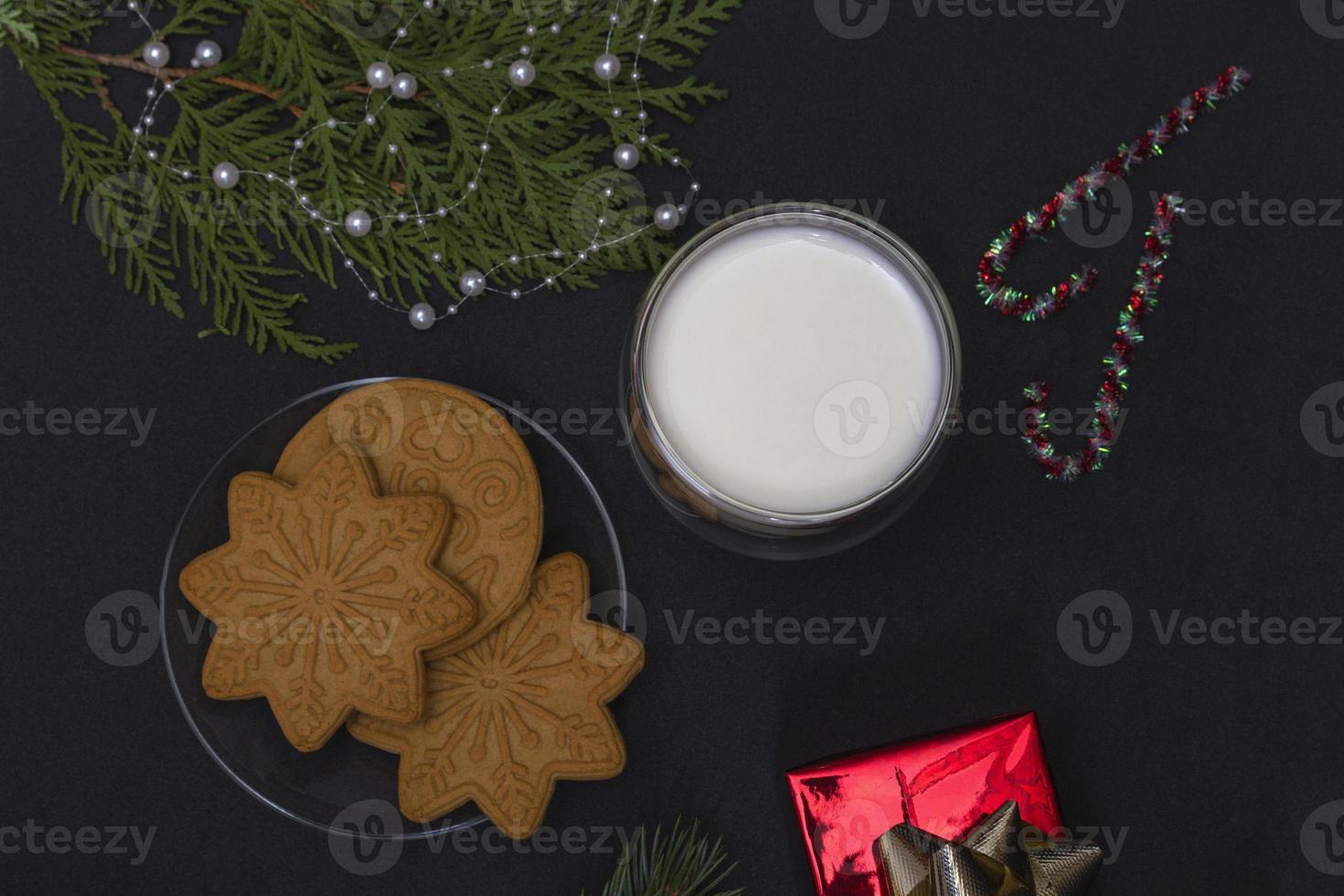 pan de jengibre y leche para santa. Composición navideña con galletas de jengibre y leche sobre un fondo negro con una rama de abeto y un regalo. foto