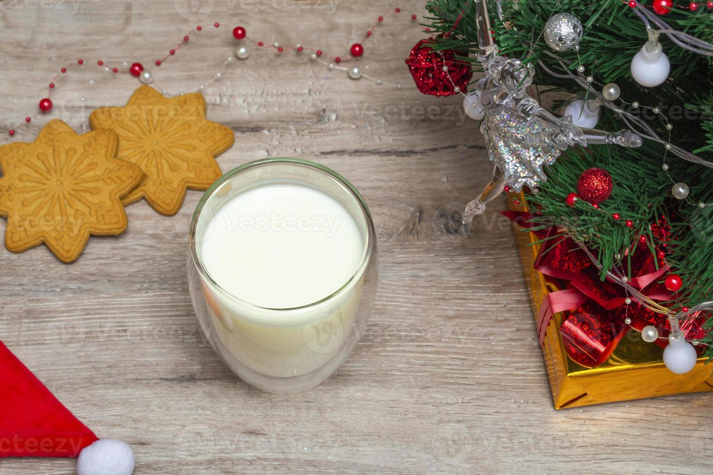 Christmas milk and gingerbread for Santa. A large glass with milk and holiday decorations. Photo of a Christmas drink on a wooden background. Close-up