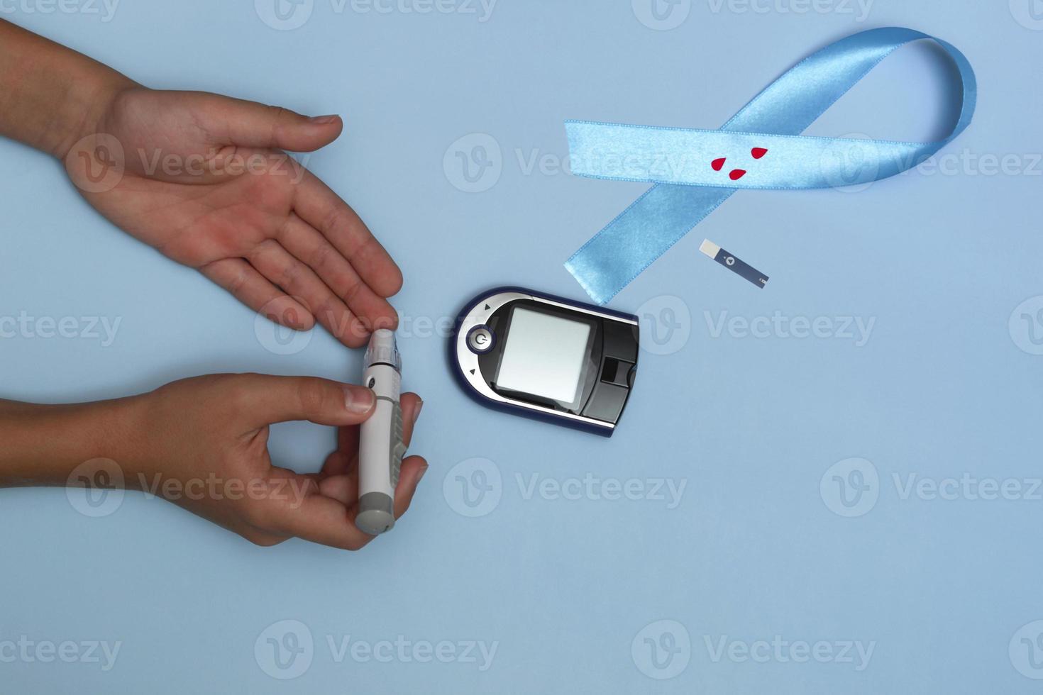 Cerrar la vista superior del concepto para el día mundial de la diabetes el 14 de noviembre. el niño mide el azúcar en sangre sobre un fondo azul y una cinta azul con gotas de sangre. foto