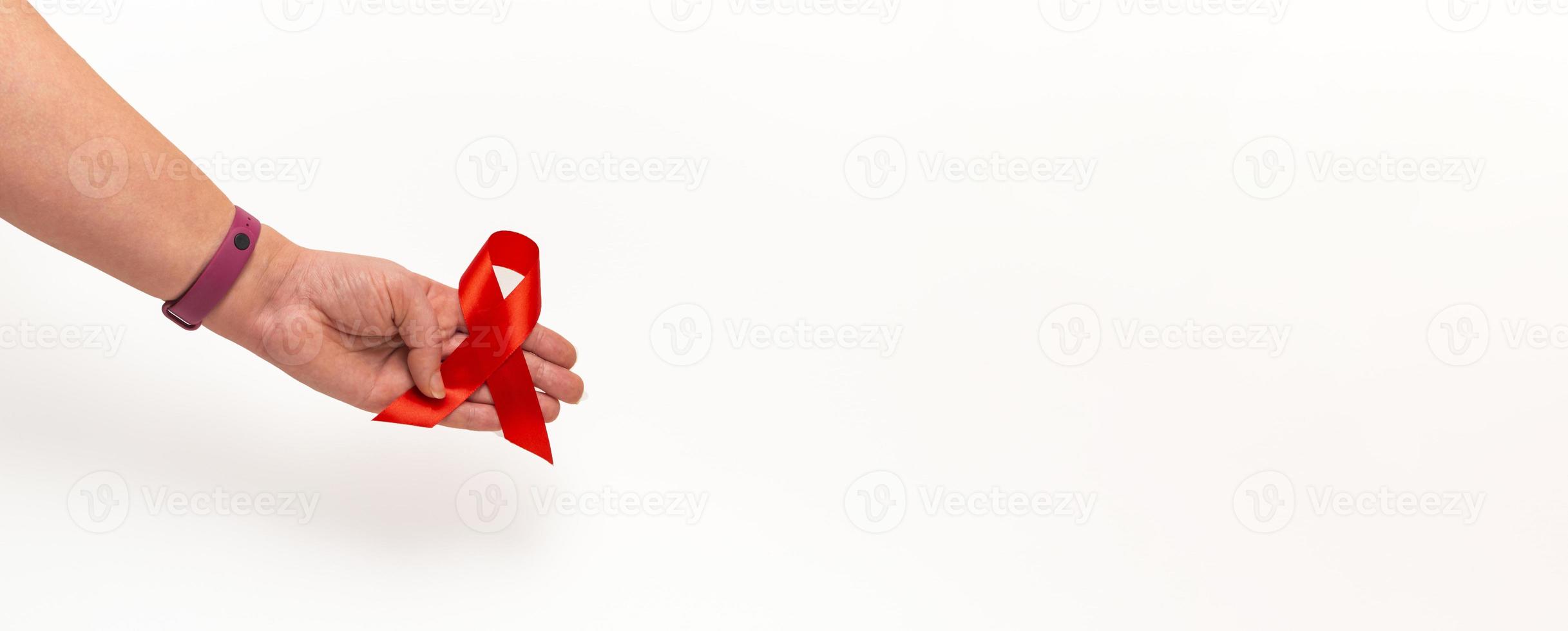 concepto médico para el día mundial del sida en diciembre. Cinta roja de concienciación sobre el sida agarrada en la mano de una mujer sobre un fondo blanco. de cerca foto