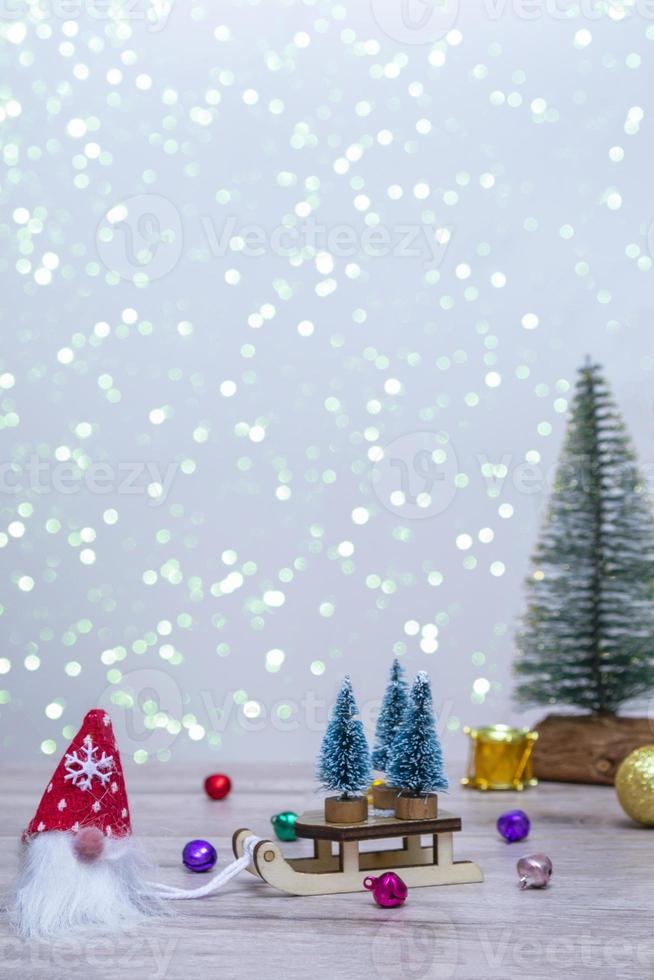 un gnomo con sombrero rojo trajo tres árboles de Navidad en un trineo. Fondo de invierno con árboles de Navidad en destellos y un ciervo. felices vacaciones. foto vertical