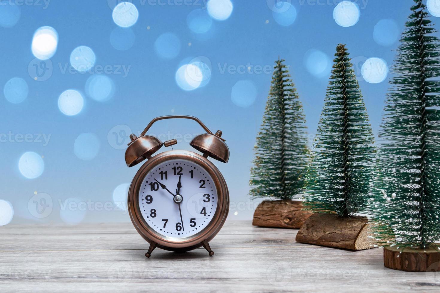 Christmas background with small Christmas trees and vintage alarm clock on a wooden background with lights. Close photo
