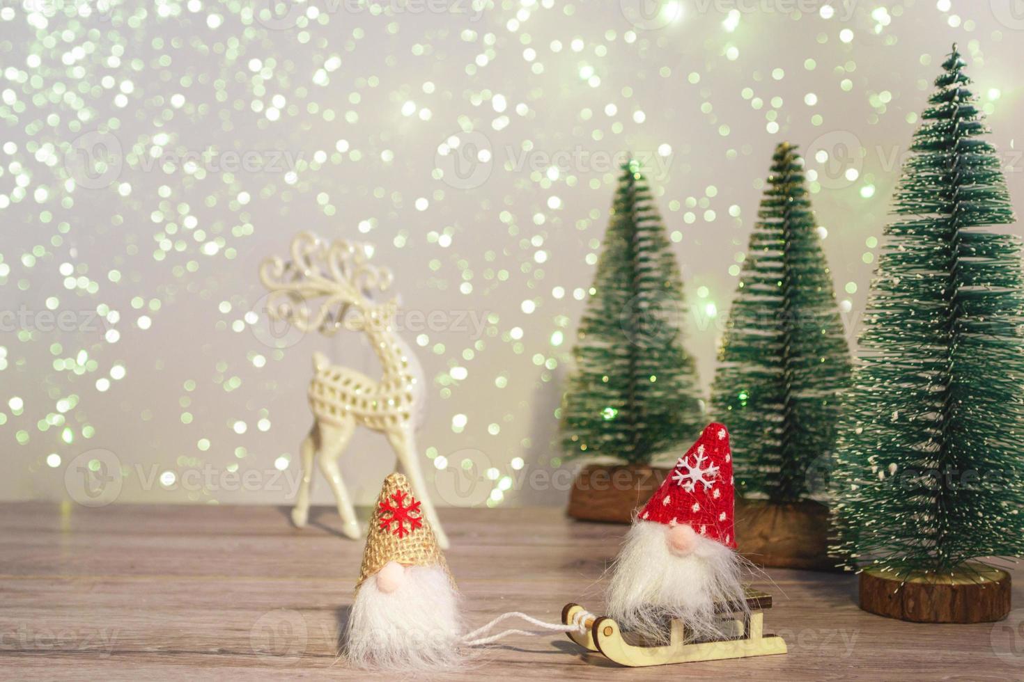 un gnomo con sombrero blanco conduce a un gnomo con sombrero rojo en un trineo. fondo de invierno árboles de navidad en destellos y un ciervo. felices vacaciones. foto