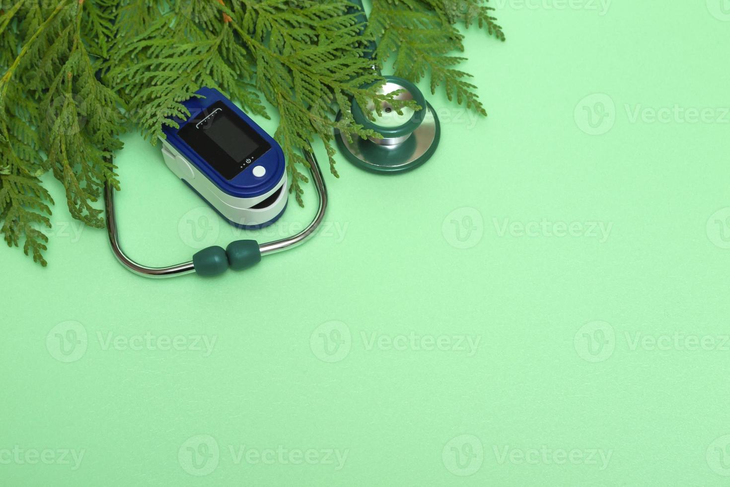 concepto médico celebrando la Navidad en la asistencia sanitaria. Vista superior de un plano sentar cerca de un estetoscopio, oxímetro de pulso con ramas de abeto sobre un fondo verde espacio de copia. foto